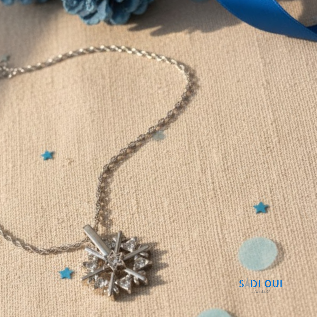 Colar Floco de Neve Brilhante Shine em aço inoxidável 304 e titânio prateado com detalhes brilhantes, em destaque sobre fundo bege com detalhes azuis, Flash Edition especial de Natal, SADI OUI Jewellery