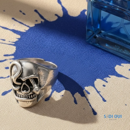 Anel Caveira Base em aço inoxidável prateado em fundo bege e azul com mancha de líquido azul
