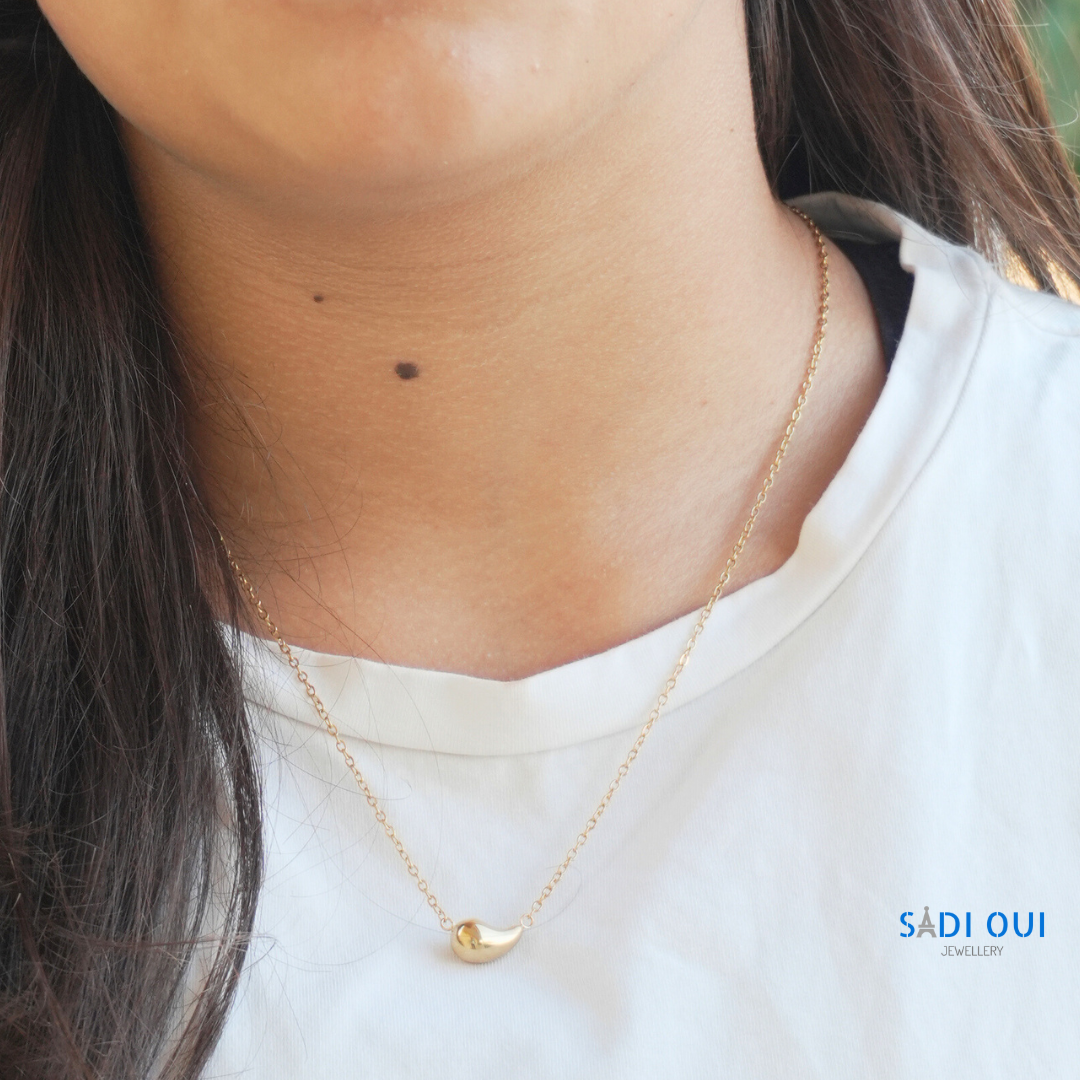 Colar Pop Drop em aço inoxidável dourado no pescoço de uma pessoa, close do pendente
